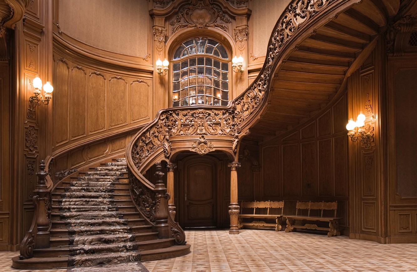 An ornate carved wooden staircase rising inside a grand private residence